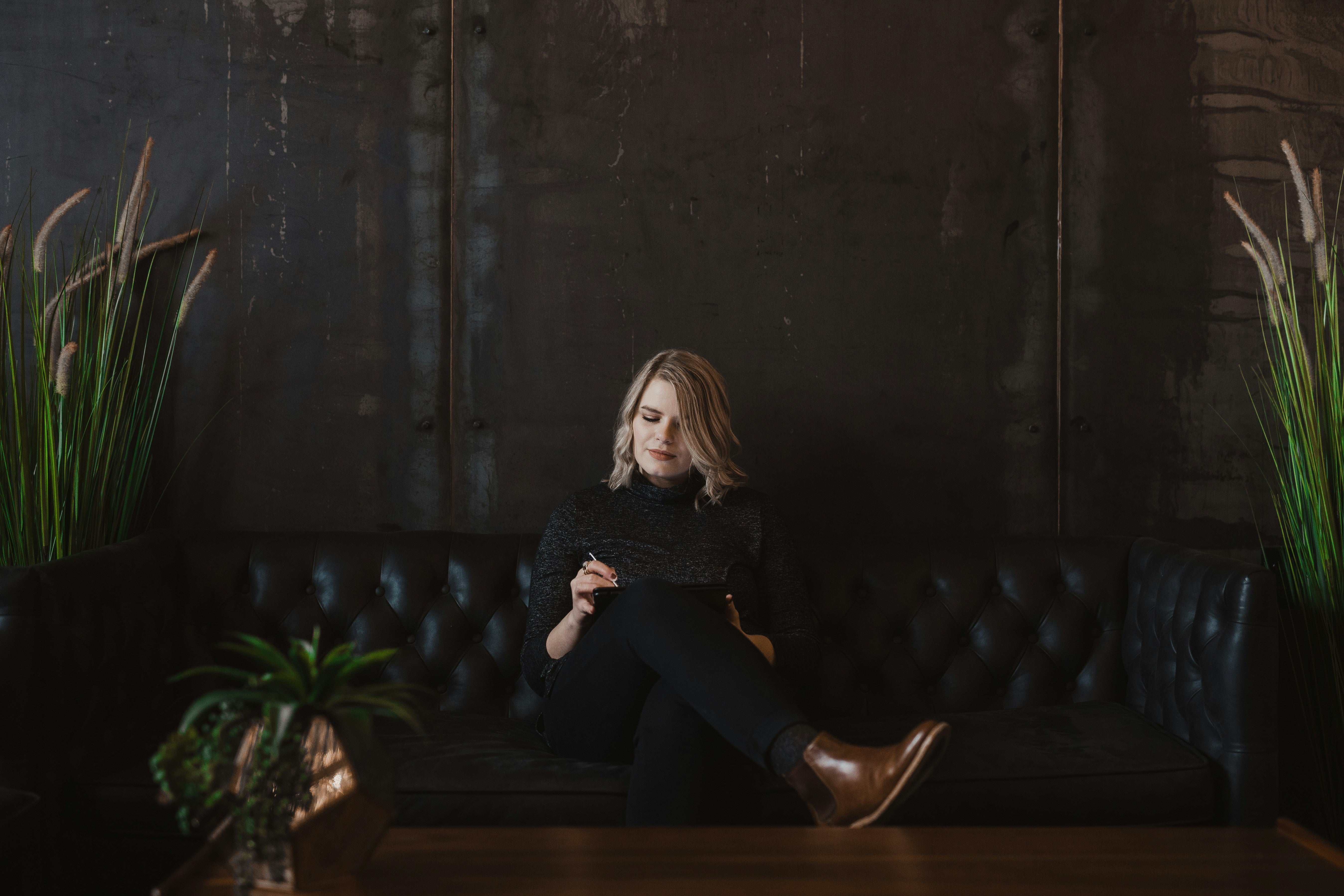 Successful woman sitting on a couch in a dark green environment.